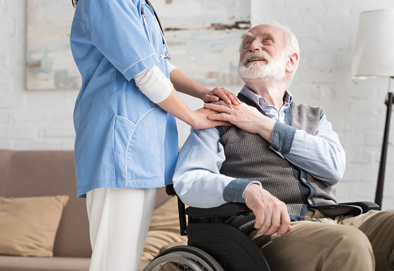 Eine Intensivpflegerin berührt einen Mann im Rollstuhl sanft an der Schulter