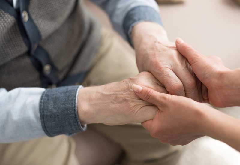 Eine Intensivpflegerin nimmt einen Pflegebedürftigen an den Händen