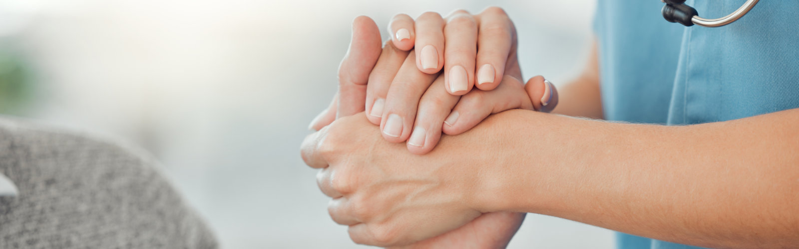 Eine Intensivpflegerin der außerklinischen Intensivpflege Unique nimmt die Hand eines Intensivpflichtigens älteren Rollstuhlfahrers