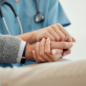 Intensivpflegerin der Außerklinischen Intensivpflege drückt die Hand eines Pflegebedürftigen