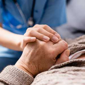 Intensivpflegerin der Außerklinischen Intensivpflege drückt die Hand eines Pflegebedürftigen